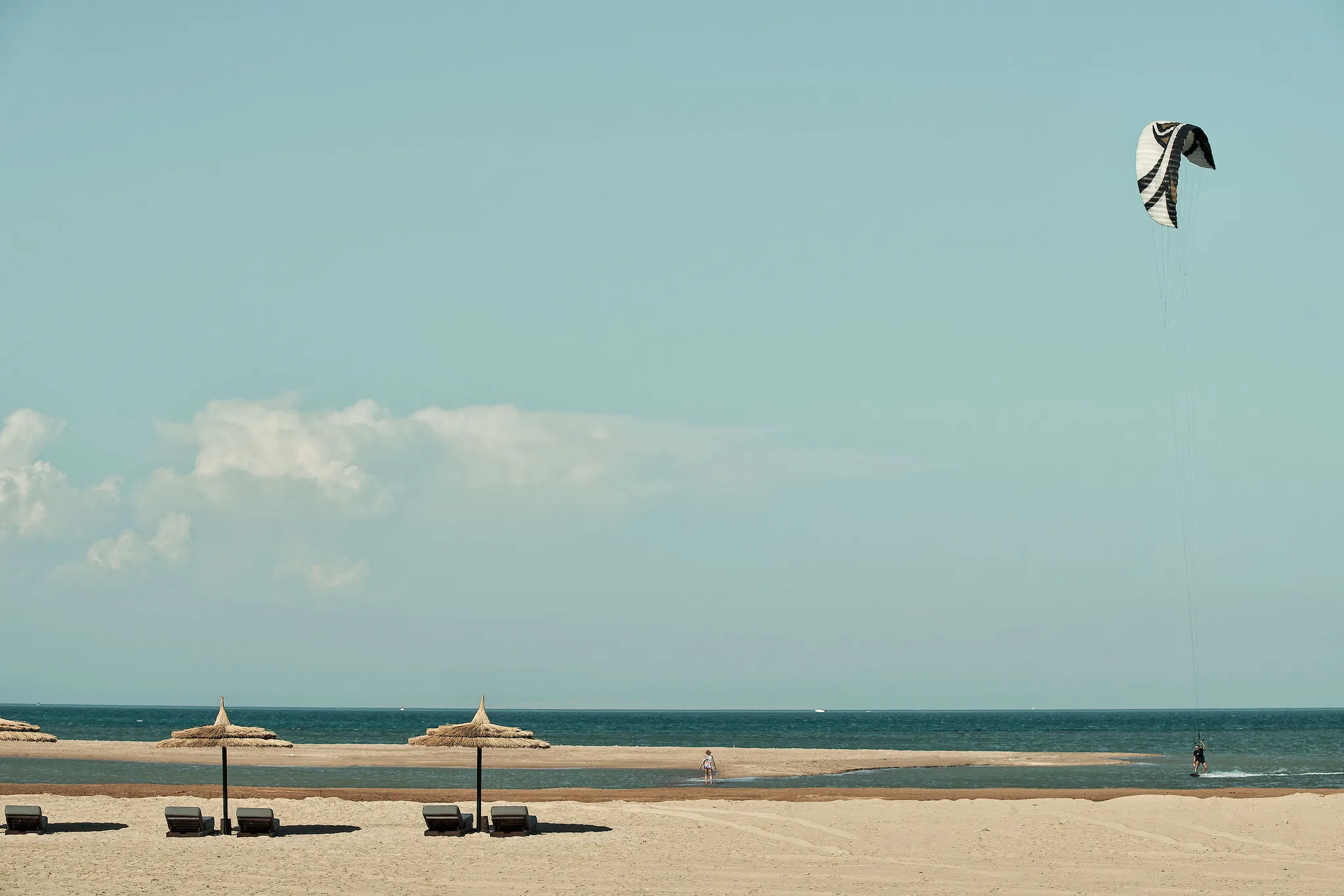 Kitesurfer gliding across the open sea near a sandy beach lined with thatched parasols and sun loungers at Casa Cook El Gouna
