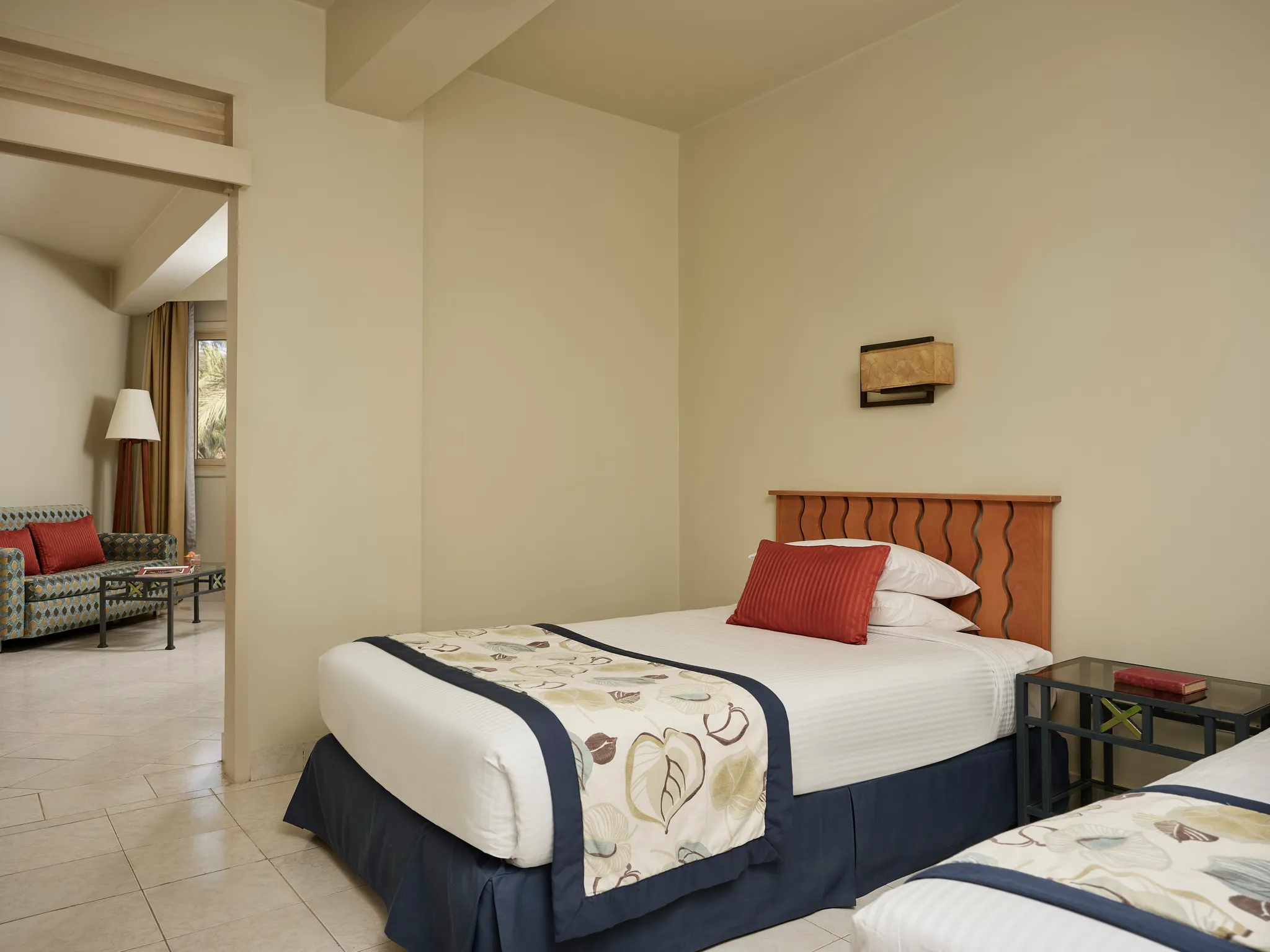 Der Schlafbereich mit zwei Einzelbetten in der Paradise Suite zeigt ein Einzelbett mit dekorativem Läufer, einen Nachttisch sowie eine Tür, die zum Wohnzimmer im Club Paradisio Hotel El Gouna führt