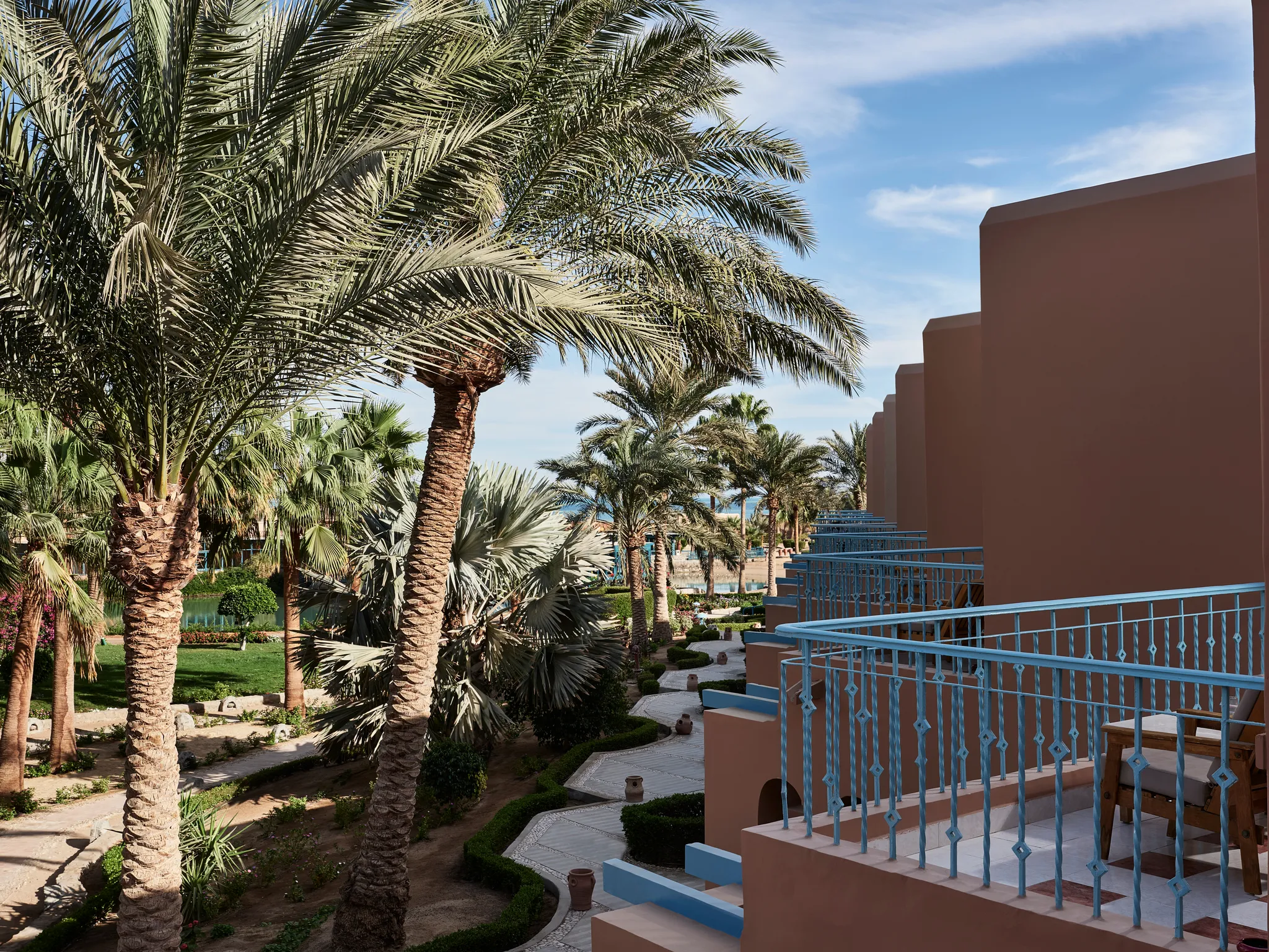 Außenansicht vom Balkon der Paradise Suite mit blauen schmiedeeisernen Geländern, üppigen Palmen und Gartenwegen im Club Paradisio Hotel El Gouna