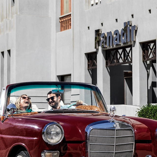 A couple enjoying a fun time in front of the Fanadir facade, seated in a vintage car.